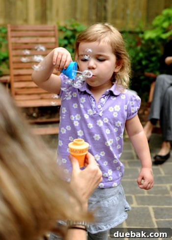 Children playing with bubble favors outdoors on the patio under clear skies.