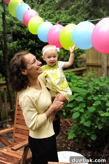 Clara and her grandmother under colorful balloon garlands at the party.