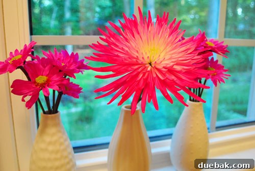 Small arrangement of repurposed bright pink flowers in a modern white vase on a windowsill