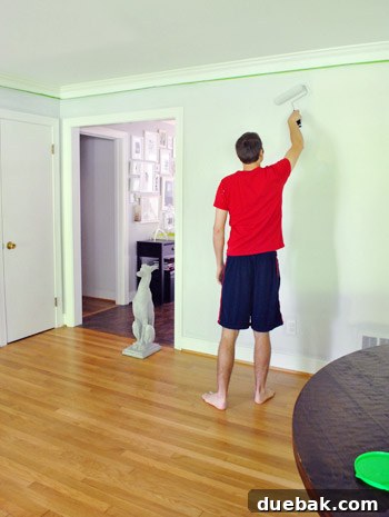 Moonshine by Benjamin Moore: The Serene Light Gray You've Been Searching For 11 A person playfully painting a wall, with an empty paint can nearby, demonstrating the lighthearted aspect of a home renovation project.