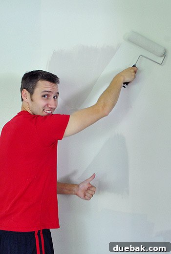 Moonshine by Benjamin Moore: The Serene Light Gray You've Been Searching For 3 A person in painting clothes, mid-stride, showcasing the progression of a DIY painting project in a dining room, before the final coat of gray paint.