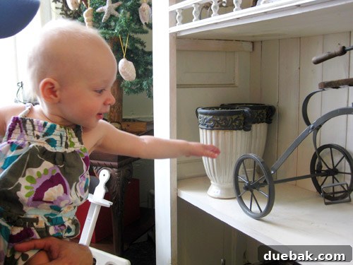 Clara, a young child, excitedly interacting with an old-fashioned metal tricycle inside The Old Screen Door shop.