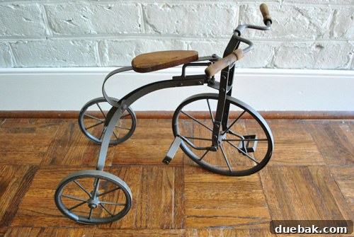 A close-up of the vintage metal tricycle purchased in Lewes, now displayed indoors, highlighting its intricate details.