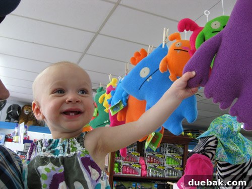 Clara, an excited child, looking up at a display of colorful monster dolls hanging from a clothesline in Kids Ketch toy store.