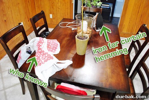 A kitchen table cluttered with various household items, including bags, mail, and craft supplies.