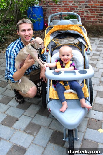Dad posing with a jogging stroller and Clara in a park