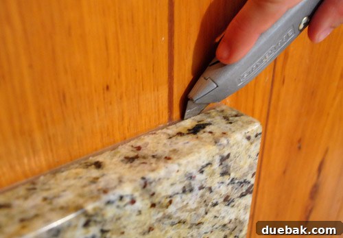 Removing Cabinets and Repairing Vinyl Flooring 14 Person using a razor to cut through silicone caulk on the kitchen desk
