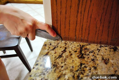 Removing Cabinets and Repairing Vinyl Flooring 16 Close-up of the desk countertop with caulk being cut, separating it from the wall and cabinet
