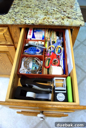 First organized kitchen drawer with office supplies like envelopes, stamps, address book, tape, stapler, pens, and scissors.