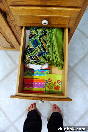 Third organized kitchen drawer showcasing neatly folded cloth napkins, runners, and paper napkins.