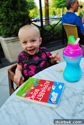 Clara with a sippy cup, Goldfish crackers, and a Dr. Seuss book on a marble table at Brio