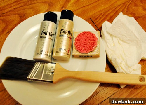 A small rubber stamper with a medallion design and two tubes of metallic craft paint (pearl white and champagne)