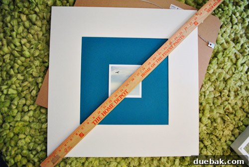 Hands carefully centering a note card onto a colored background within a frame