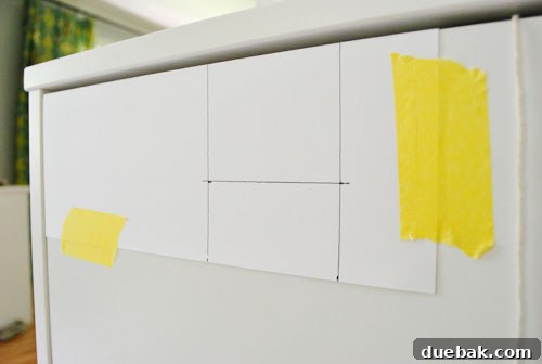 Clever Printer Concealment Ideas 4 Detailed view of a DIY card stock template with precise measurements for drilling cabinet handle holes, laid over a cabinet door.