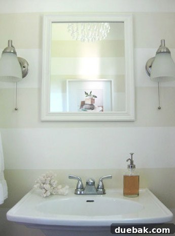 Charming hall bathroom in the first house with striped walls, a glass chandelier, and pedestal sink