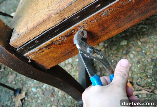 Hand using channel lock pliers to remove upholstery staples from wood frame