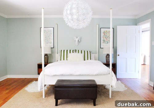 A wide shot of a bedroom side, showing a mid-century nightstand with a lamp and artwork, indicating an unfinished but evolving space.
