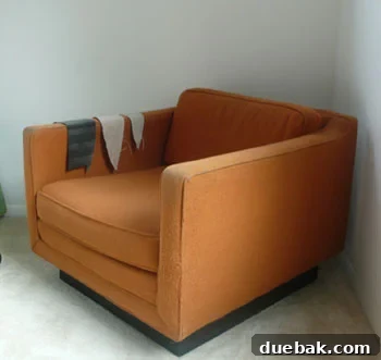 Old chair awaiting reupholstery with worn orange fabric, highlighting its dated appearance.