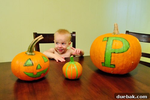 A toddler in a diaper standing next to paints and pumpkins