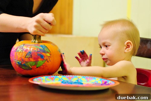 Close-up of a toddler's hand covered in paint, dabbing a pumpkin