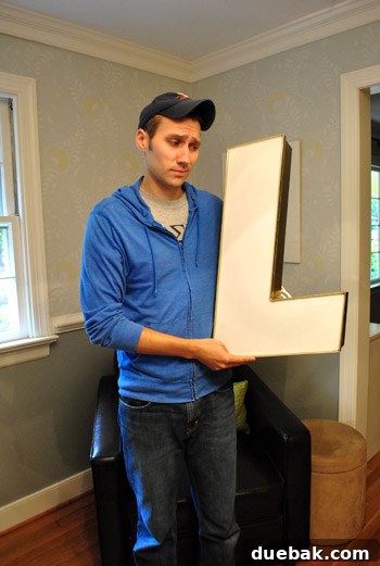 A large, vintage industrial letter 'L' leaning against a white wall in a home setting, appearing ready for display.