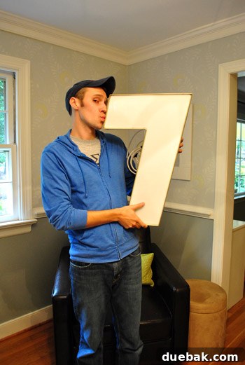 A man playfully snuggling the large industrial number '7' with a joyful expression, suggesting a deep affection for the unique decor piece.
