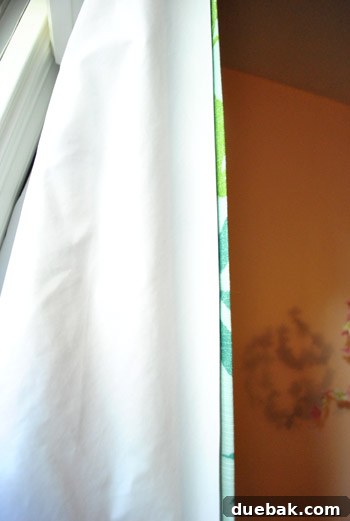 Craft Your Own Blackout Curtains 2 Close-up of a DIY no-sew blackout curtain liner peeking from behind a patterned curtain panel in a child's nursery, highlighting the simplicity and effectiveness of the layering method.