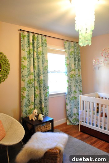 Craft Your Own Blackout Curtains 4 Baby girl's pink nursery featuring colorful blue and green floral curtains that subtly conceal the newly installed hidden DIY blackout curtain liners, creating a darker sleep environment.