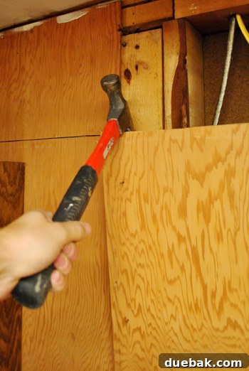 Man prying off a section of cut plywood from the kitchen wall