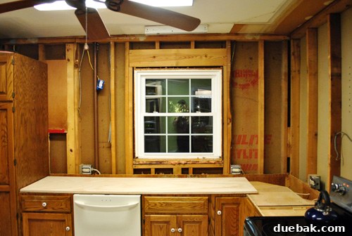 Kitchen walls completely stripped, showing exposed studs