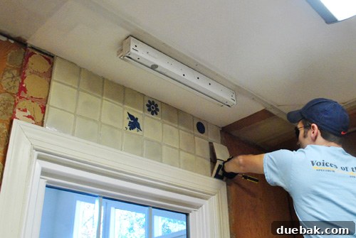 Kitchen wall with partial backsplash removed, showing exposed plywood