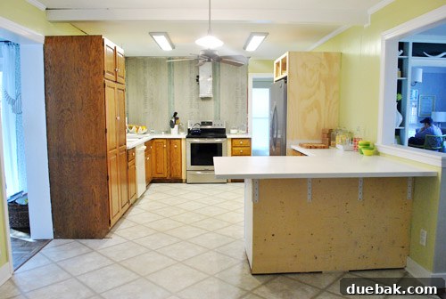 A modern kitchen peninsula awaiting stools, showcasing recently installed countertops and empty space.