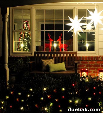 Our Dazzling Outdoor Christmas Display 4 A slightly wider view of the porch, highlighting the varied heights of the hanging stars and the bright red and white lights adorning the bushes leading to the front door.