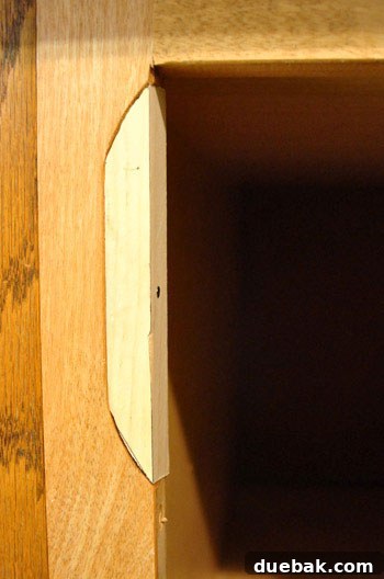 Repaired cabinet frame with jigsawed wood pieces filling old hinge notches.