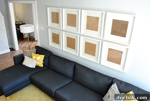 A living room wall with several picture frames being arranged, showing the process of creating a gallery wall.