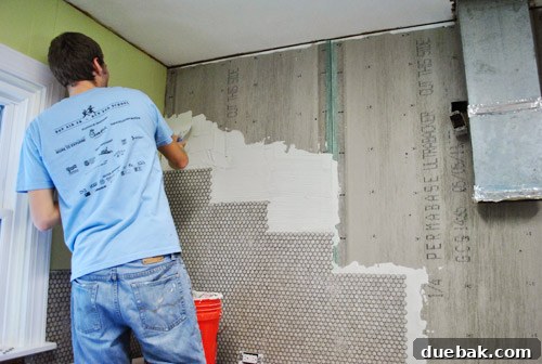John applying thinset to the kitchen wall using a putty knife before tiling