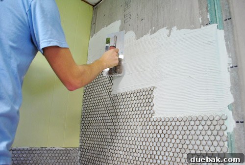 Close-up of a notched trowel creating ridges in thinset on the kitchen wall