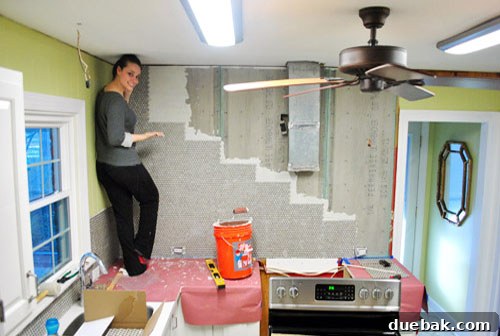 Woman standing on kitchen counter placing the top penny tile on the wall
