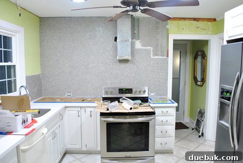 Progress shot of the kitchen wall being gradually covered with penny tiles