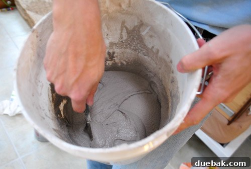 Applying grout to penny tiles using a rubber float, spreading it evenly across the surface.