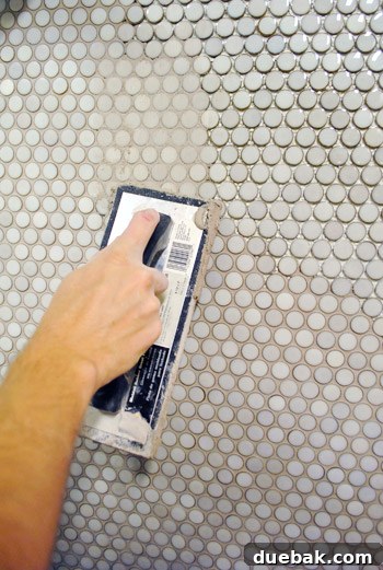 Applying grout to penny tiles with a rubber float, ensuring all gaps are filled.