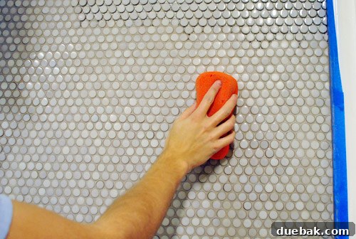 Cleaning excess grout from penny tiles with a wet sponge, smoothing the grout lines.