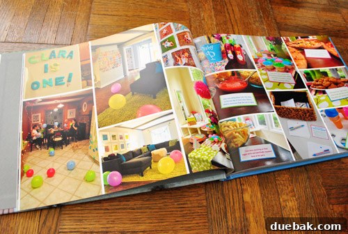 Two pages of a photo book showing pictures from Clara's 1st birthday party, including a glimpse of a dark kitchen