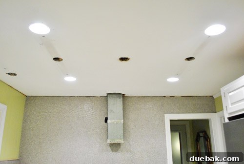 Kitchen ceiling showing four newly installed recessed can lights, replacing old fixtures, emphasizing improved lighting