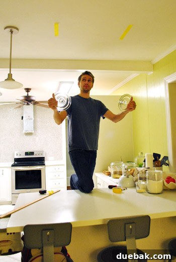 Man holding cereal jar lids to ceiling to visualize pendant light placement for kitchen island
