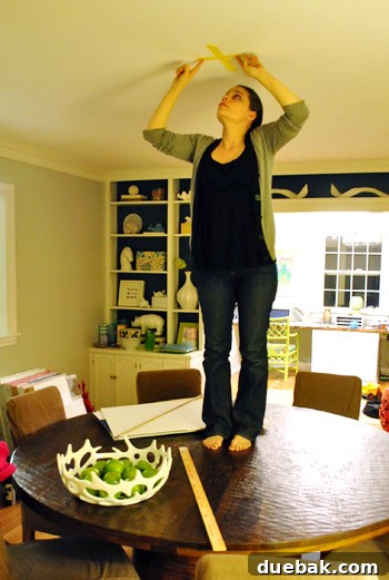Person on a dining table marking the ceiling for a new light fixture in the dining room