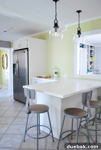 Elevating Kitchen Style with Twin Glass Pendants 12 A wider view of the kitchen area, showing the fridge and a wall with natural light