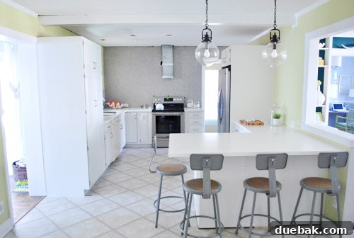 Elevating Kitchen Style with Twin Glass Pendants 8 Wider view of the kitchen and living room, highlighting the peninsula and the 'cozy corner' by the fireplace