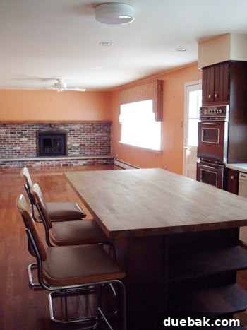 Outdated living room before renovation with dark orange wood paneling on walls and carpeted floor
