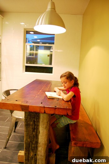 Transformed kitchen featuring a custom-built slim table and reclaimed wood details, illuminated by recessed lighting